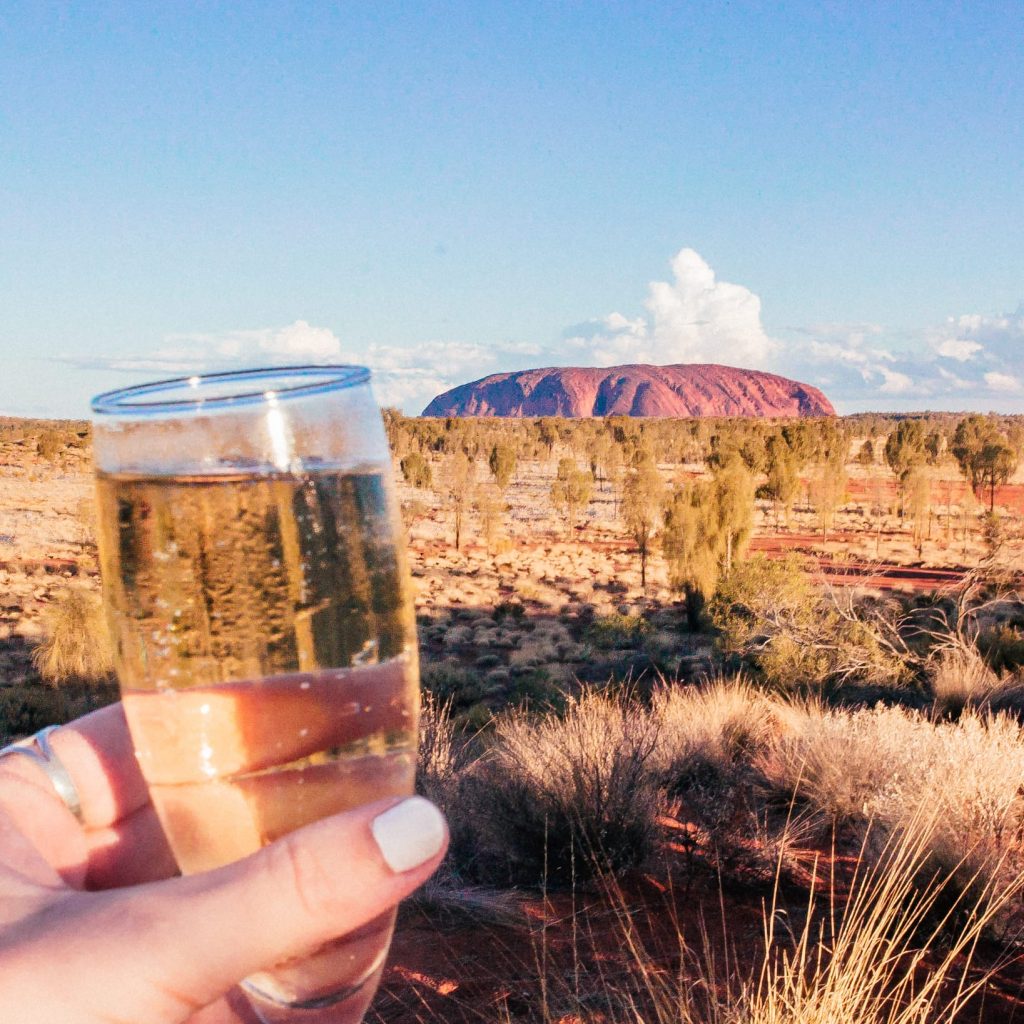 Raising a glass of champagne to Uluru in the distance at sunset